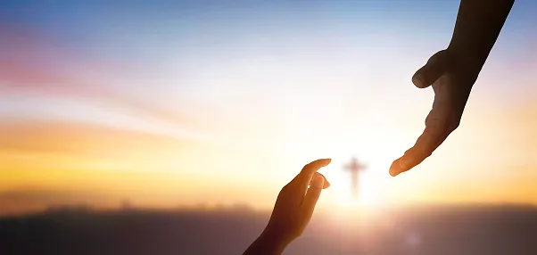 adult hand reaching down to child's hand with cross in the background